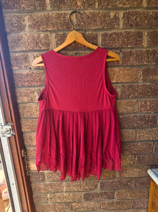 Next burgundy vest top on wooden hanger against brick wall showing pleated chiffon back panel with pointed hem