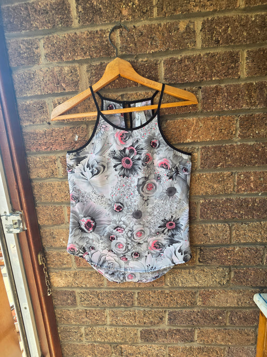 Iron and Flint grey and pink floral cami top with cage back on wooden hanger against brick wall, front view