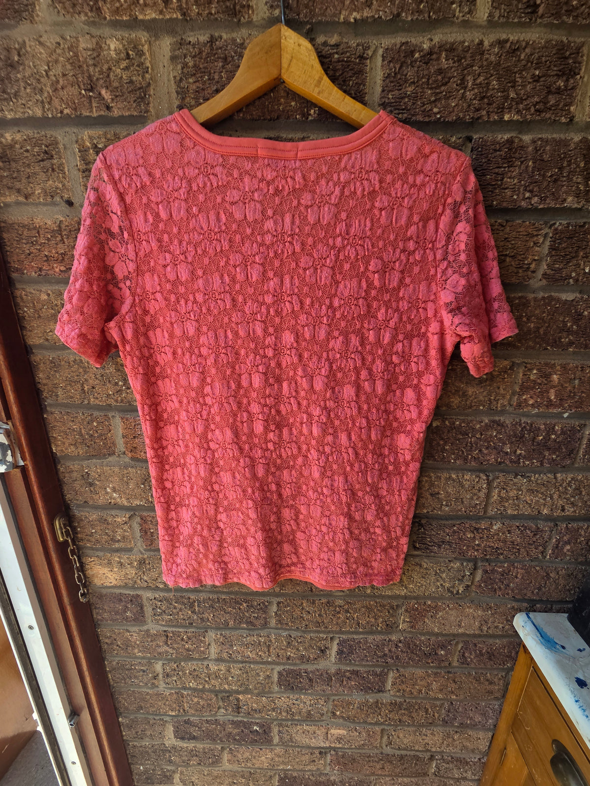 Paramour coral pink floral lace top on wooden hanger against brick wall, back view