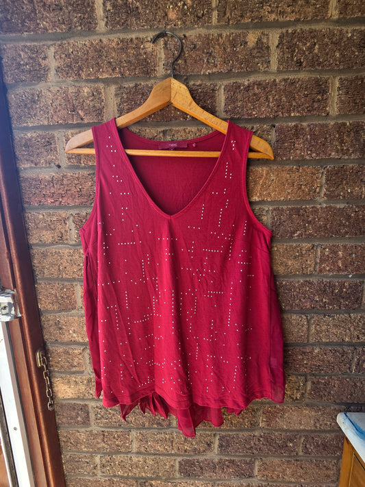 Next burgundy embellished vest top on wooden hanger against brick wall showing silver stud detail across front